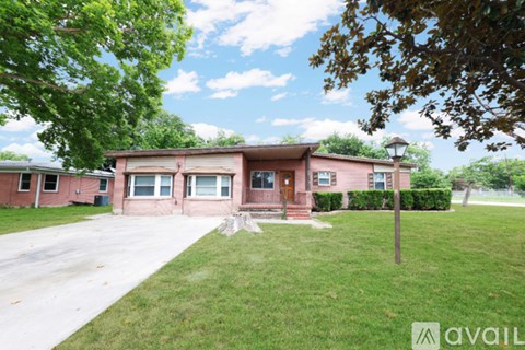 A house with a red brick exterior and a brown roof is surrounded by a grassy lawn and trees.