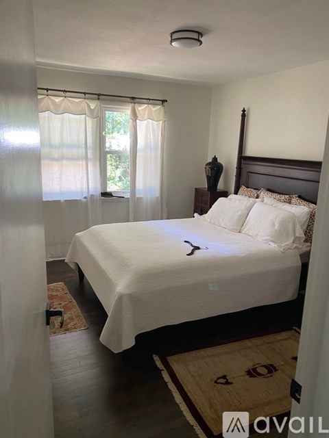 A bedroom with a bed, nightstand, and window with curtains.