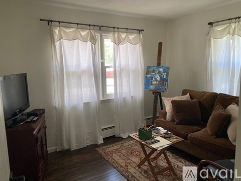 A living room with a brown couch, a wooden cabinet, a television, a rug, and a painting on a stand.