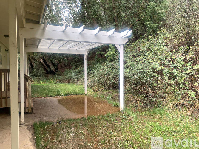 A white pergola is attached to a building and extends over a concrete path.