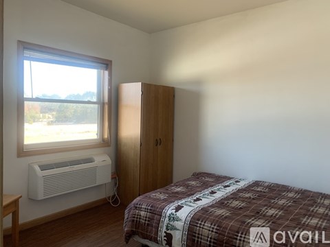 A bedroom with a bed, a window with an air conditioner, and a wardrobe.