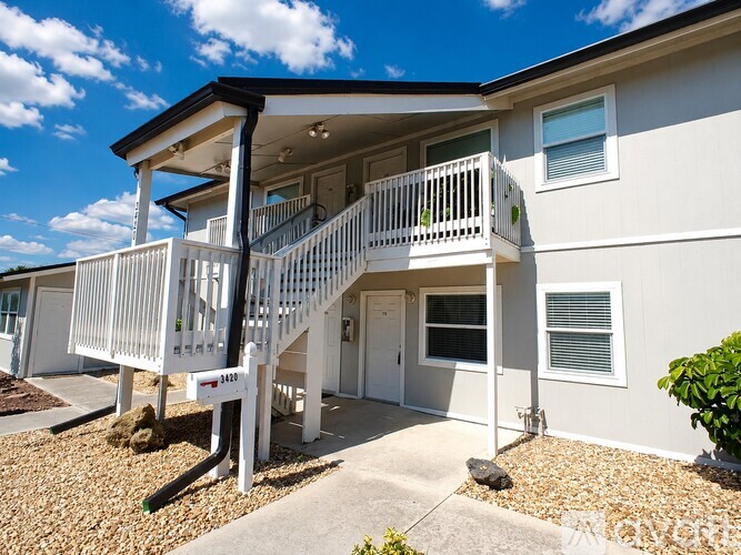 A white two-story house with a balcony and a small garden in front.