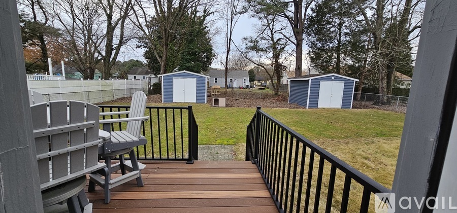 A deck with a black railing and a grey chair overlooks a grassy area with two blue sheds.