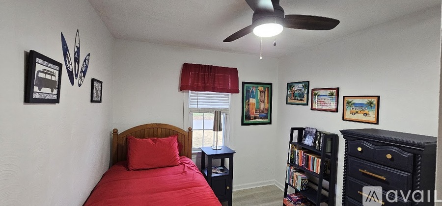 A bedroom with a red bed and a ceiling fan.