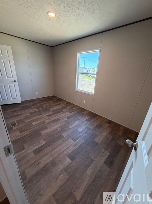 A room with wooden flooring and a window showing a view of a building.