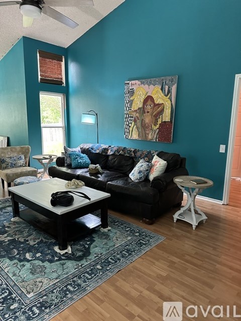 A living room with a black couch, a coffee table, and a painting on the wall.