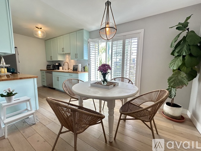 A kitchen with a table and chairs in the foreground and a plant on the side table.