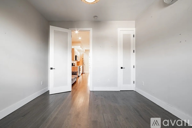 A room with a wooden floor and white walls, leading to another room.