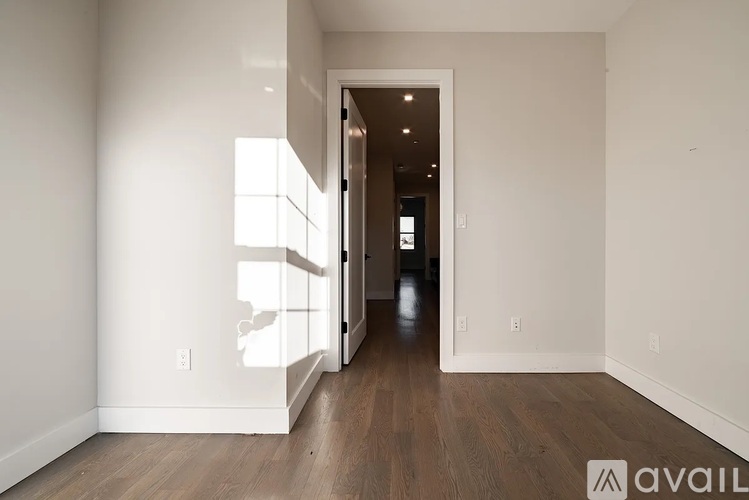 A hallway with wooden floors and white walls leading to a door.