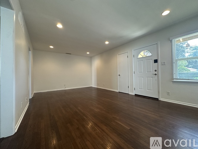 A room with wooden floors and white walls, with a window on the right side.
