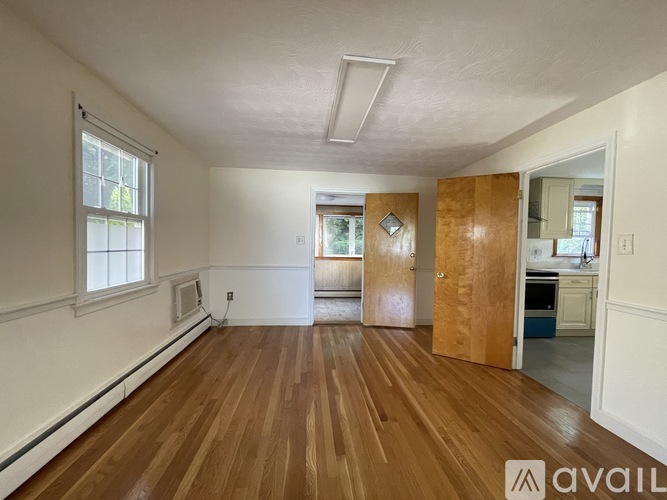 A room with wooden flooring and white walls, with a doorway leading to another room.