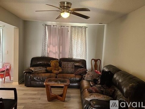 A living room with a brown leather couch and a ceiling fan.