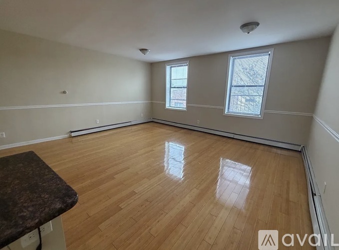 A spacious room with wooden flooring and two windows.