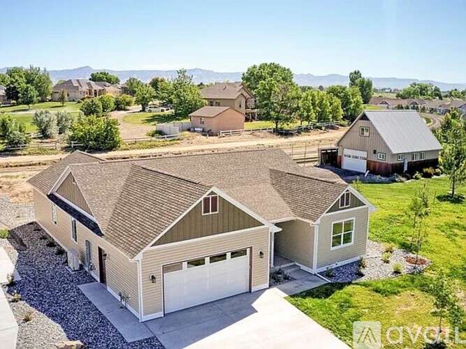 A large house with a garage is surrounded by a gravel driveway and a grassy lawn.