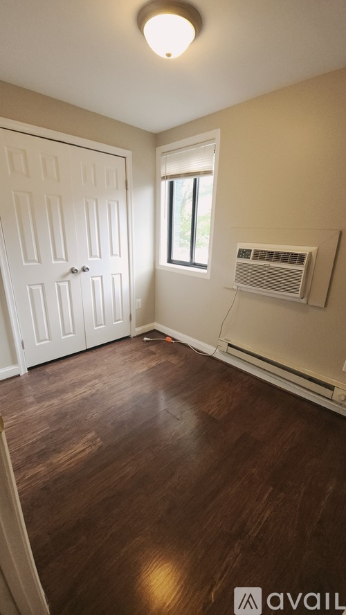 A room with a white door and a window with an air conditioner unit on the wall.