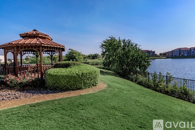 A gazebo sits in a grassy area next to a lake.