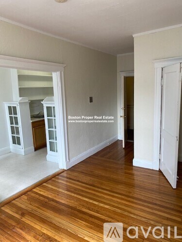 A room with wooden floors and white walls, with a door on the right and a window on the left.
