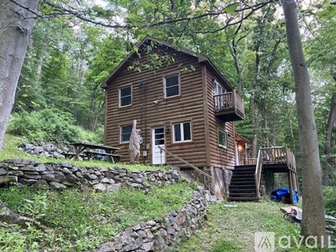 A wooden cabin in the woods with a stone wall and a car parked in front.