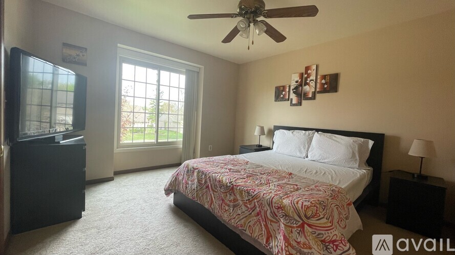 A bedroom with a bed, a ceiling fan, and a window with a view of the outdoors.