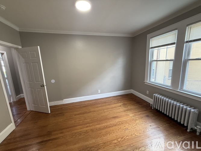 A room with a white door, a window with blinds, and a radiator on the floor.