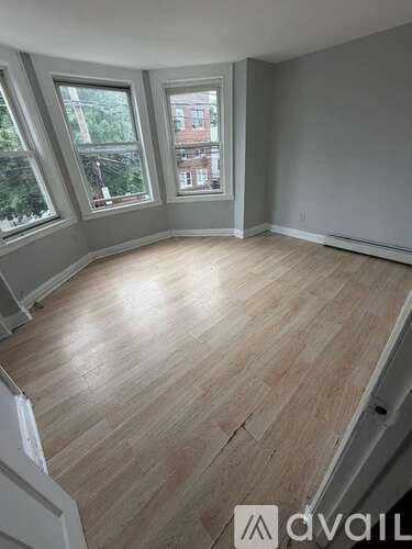 A room with wooden flooring and three windows.
