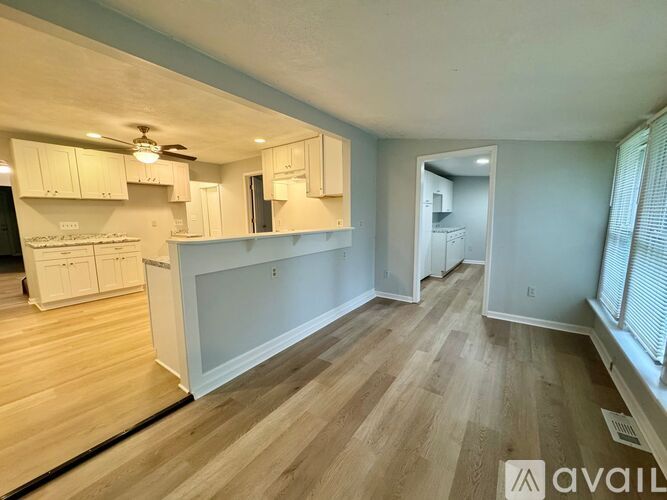 A spacious kitchen and living room with wooden flooring and white cabinetry.