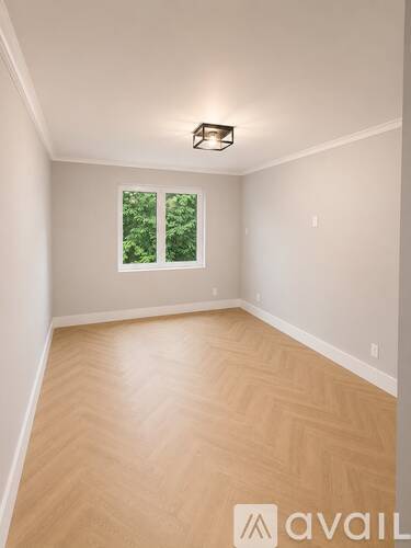 A room with wooden flooring and a window showing greenery outside.