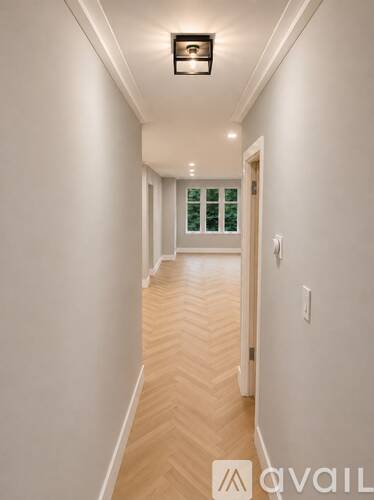 A long hallway with a light on the ceiling and a door at the end.