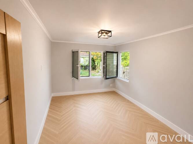 A room with wooden flooring and a window with a view of greenery outside.