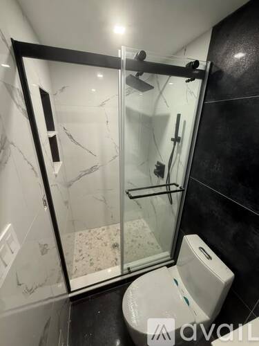 A white toilet with a glass door shower in a black and white bathroom.