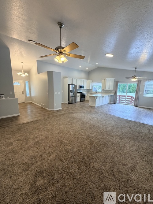 A spacious living room with a ceiling fan and carpeted floor.