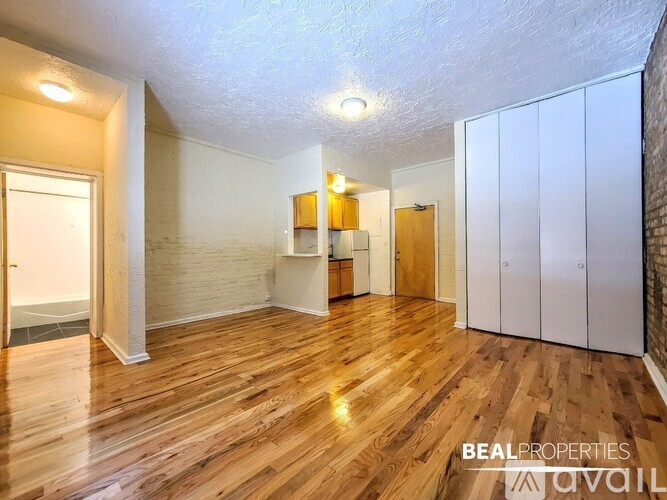 A spacious room with wooden flooring and white walls, featuring a kitchenette with a sink and cabinets.