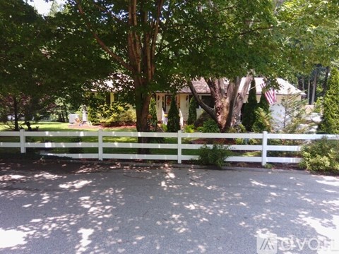 A white fence surrounds a tree in front of a house.