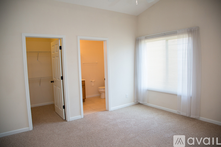 A room with a carpeted floor and a window with white curtains.
