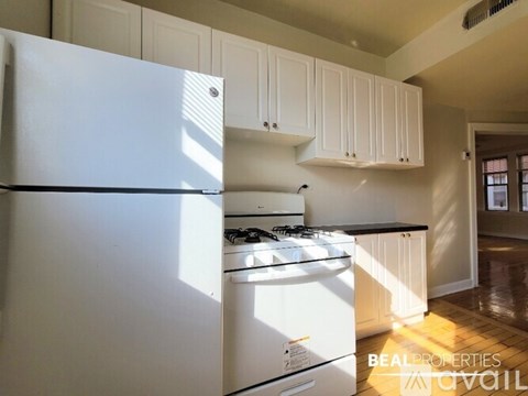 A white refrigerator is in a kitchen with white cabinets.