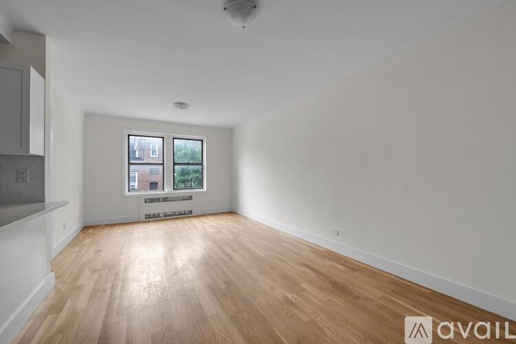 A spacious room with wooden flooring and a window showing a view of buildings and trees.