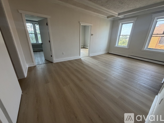 A spacious room with wooden floors and two windows.