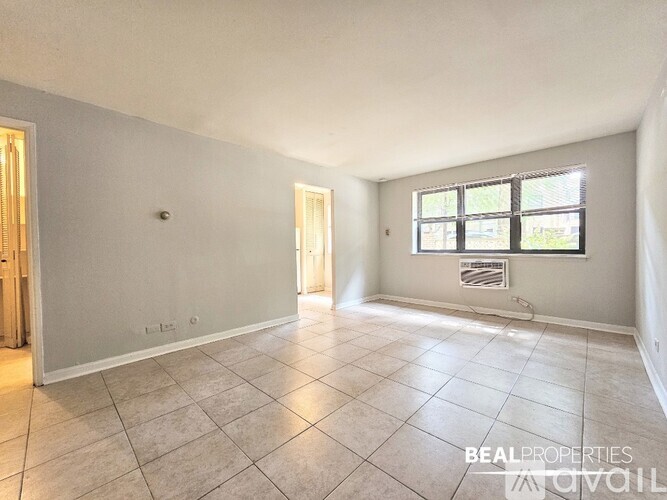 A spacious room with tiled flooring and a window with blinds.