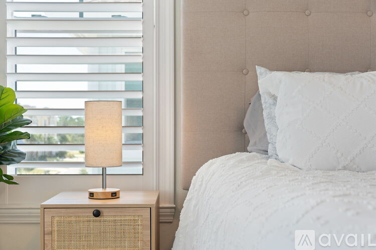 A bedroom with a white bed and a lamp on a wooden nightstand.