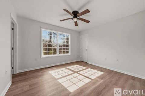 A room with a ceiling fan and a window with a view of trees.