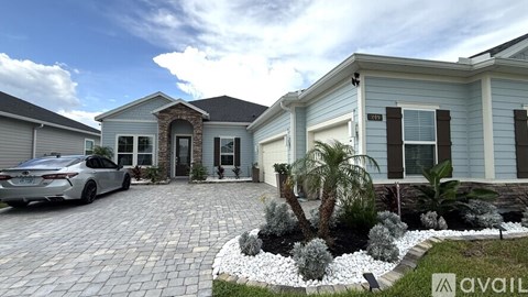 A house with a car parked in front and a garden with white flowers and a palm tree.