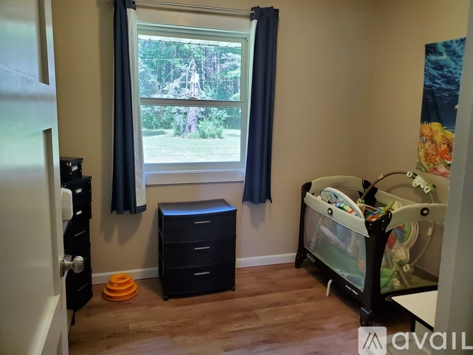 A baby's room with a crib, dresser, and a window with a view of trees.