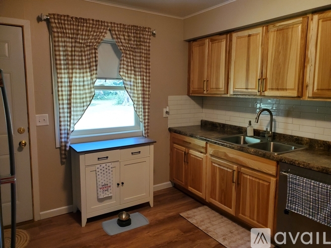 A kitchen with wooden cabinets and a checkered curtain.