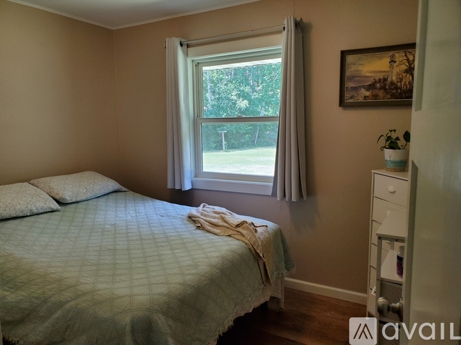 A bedroom with a bed, a nightstand, and a window with curtains.