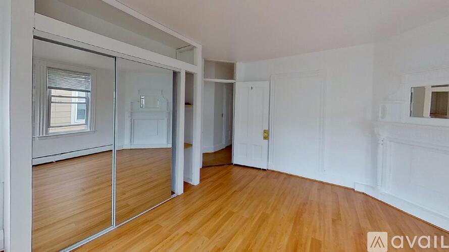A room with wooden floors and white walls, with a glass door leading to a balcony.