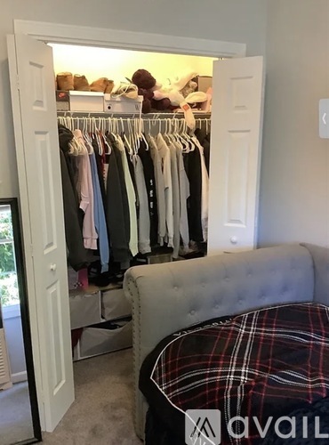 A bedroom with a bed, a couch, and a wardrobe with clothes hanging.