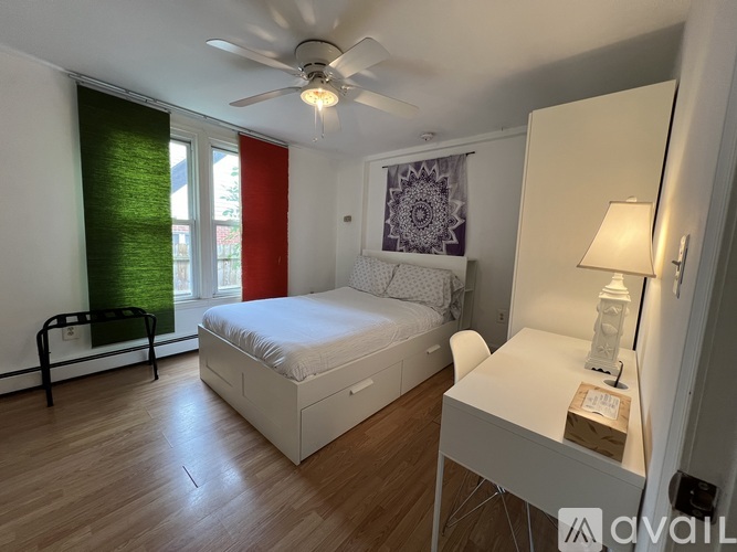 A bedroom with a bed, desk, and window with red and green curtains.