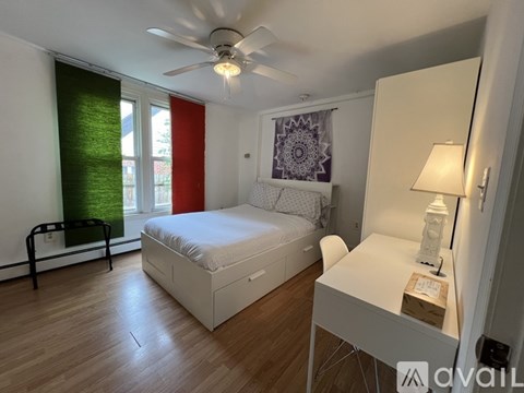 A bedroom with a bed, desk, and window with red and green curtains.