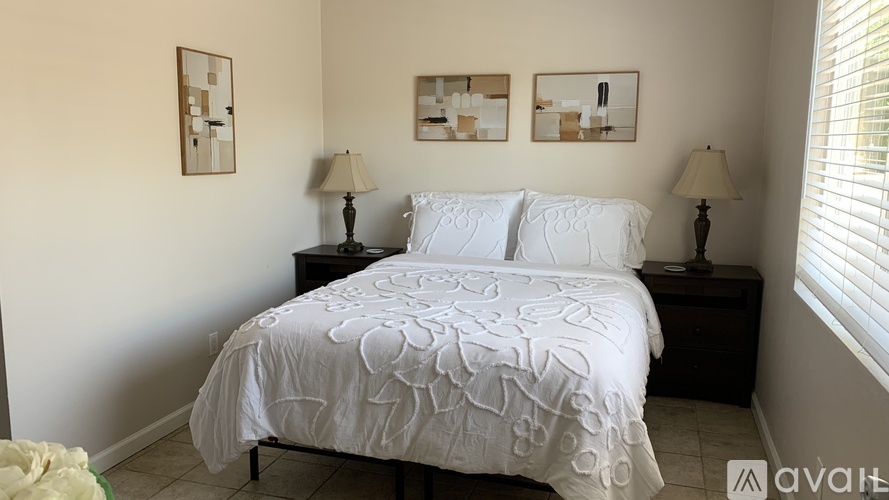 A bedroom with a bed, two lamps, and two pictures on the wall.