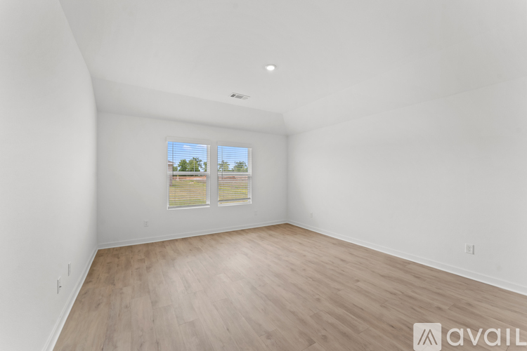 A room with wooden flooring and a window showing a view of trees.
